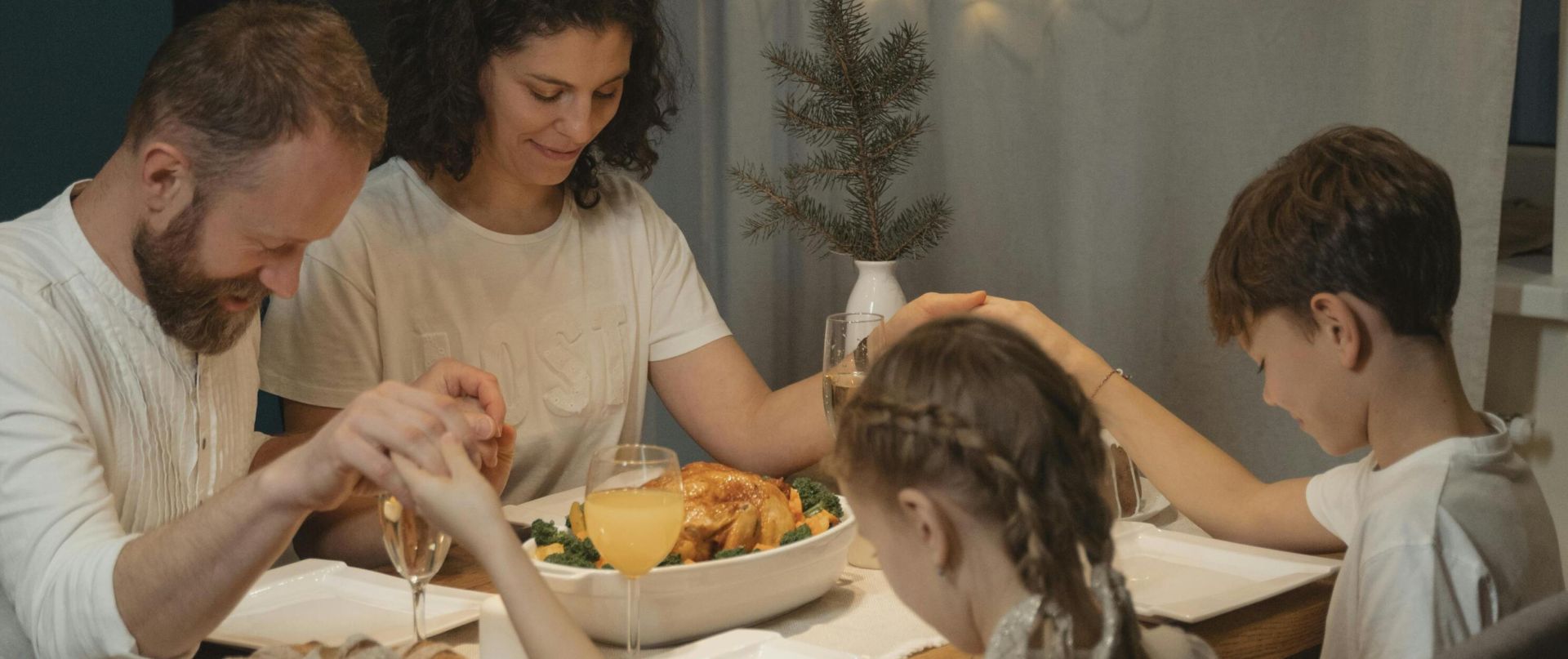 A family holding hands and praying around a festive dinner table set with food and decorations.
