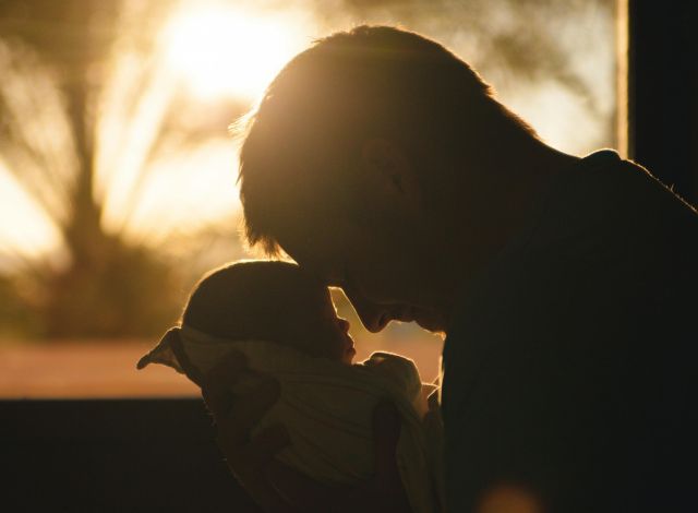 Silhouette of a father holding his newborn at sunset, highlighting love and connection.