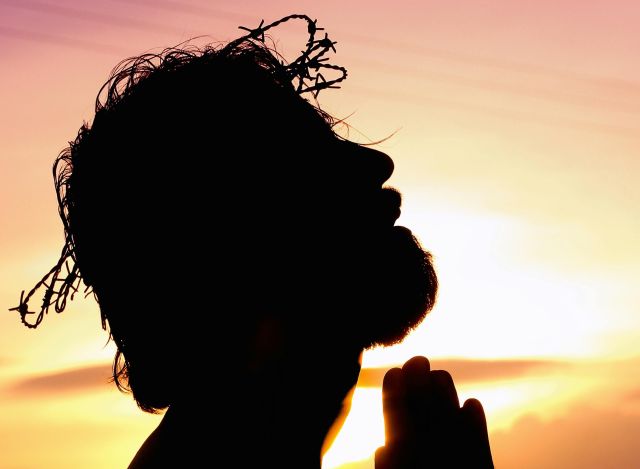 A silhouette of a man praying at sunset, wearing a crown of thorns, symbolizing faith and hope.
