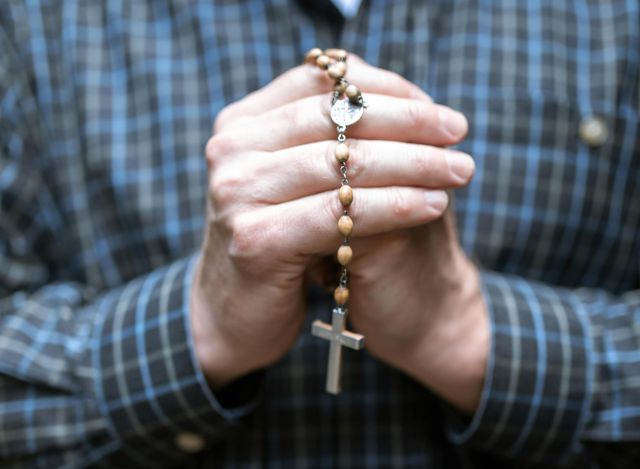 Close-up of a man holding rosary beads in prayer. Focus on faith and contemplation.