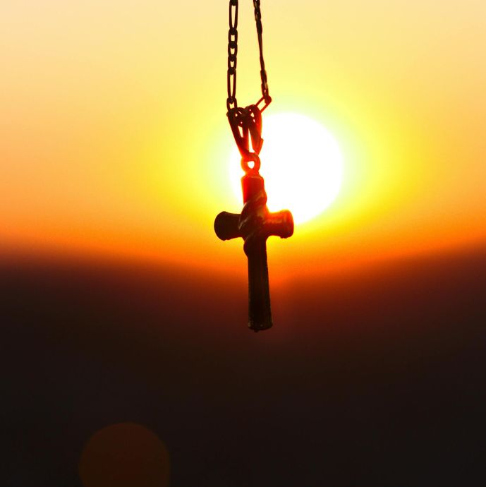 A cross pendant silhouetted against a vibrant sunset, symbolizing faith and peace.